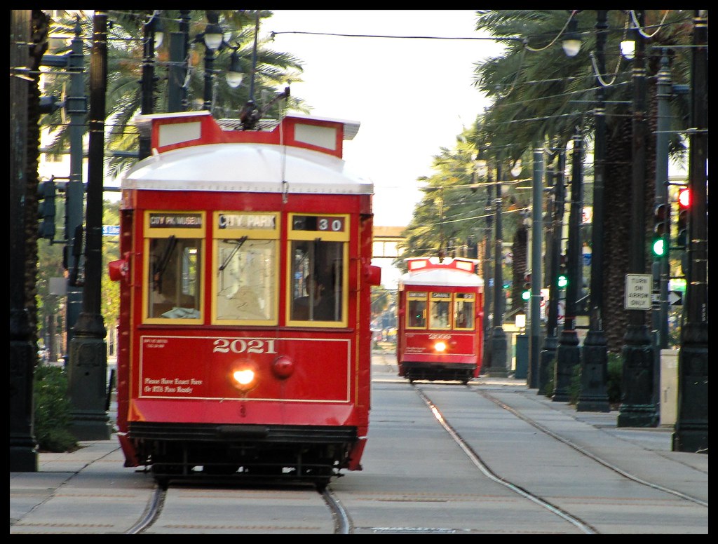 Two red street cars going down a tree lined street.
